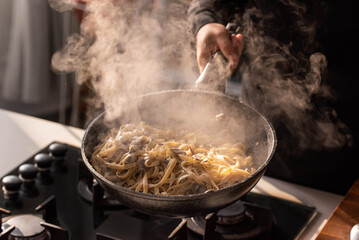 Professional chef cook making Italian Tagliatelle pasta with mushrooms and cream at kitchen gas stove in wok pan. Flying pasta levitation in motion.