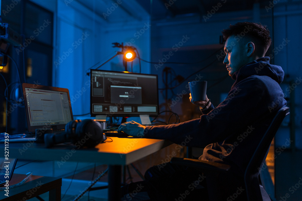 Poster cybercrime, hacking and technology concept - male hacker in dark room drinking coffee and using comp
