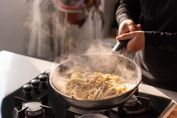 Professional chef cook making Italian Tagliatelle pasta with mushrooms and cream at kitchen gas stove in wok pan. Flying pasta levitation in motion.