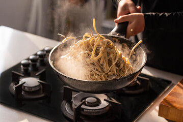 Professional chef cook making Italian Tagliatelle pasta with mushrooms and cream at kitchen gas stove in wok pan. Flying pasta levitation in motion. - obrazy, fototapety, plakaty