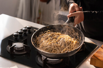 Professional chef cook making Italian Tagliatelle pasta with mushrooms and cream at kitchen gas stove in wok pan. Flying pasta levitation in motion.
