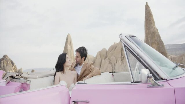 Elegant photo shoot of the newlyweds. Action.A beautiful slender girl in a white long dress with her man posing for the camera on the street next to the car and in a heated room with a bed.