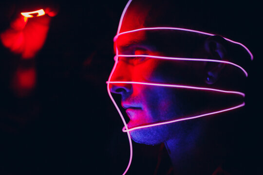 Portrait Of Man With Neon Glow Tube Lines On His Face In Dark. Concept Cyberpunk And Virtual Reality