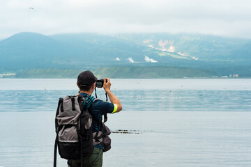 Obraz premium male tourist with a backpack photographs a foggy sea bay