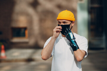 Young disabled man with artificial prosthetic hand wearing medical protective face mask