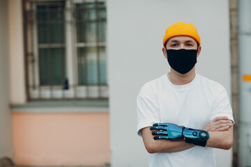 Young disabled man with artificial prosthetic hand wearing medical protective face mask