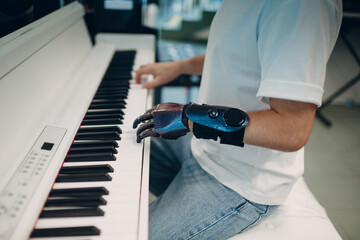 Young disabled man play on piano electronic synthesizer with artificial prosthetic hand in music...