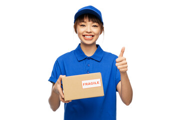 profession, job and people concept - happy smiling delivery woman in blue uniform holding parcel box with fragile mark showing thumbs up gesture over white background