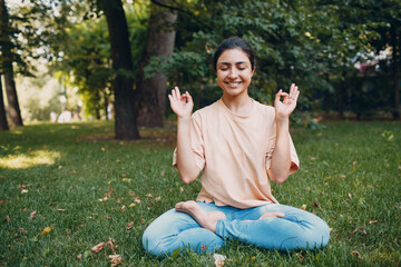 Indian woman doing yoga and meditation in lotus asana pose in outdoor summer park.