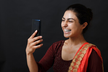 Happy indian woman having video call on mobile phone. Brunette in traditional sari clothes of red...