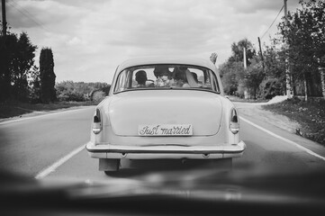 Happy bride kiss groom, newlywed wedding couple is driving a retro car on a country road for...