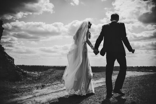 The bride and groom walk back on the nature. Portrait of an attractive couple in country. Wedding ceremony. Newlyweds getting married outdoors. Black and white photo.