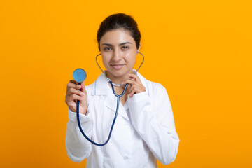 Portrait of indian doctor woman in white medical gown stethoscope isolated on yellow background.