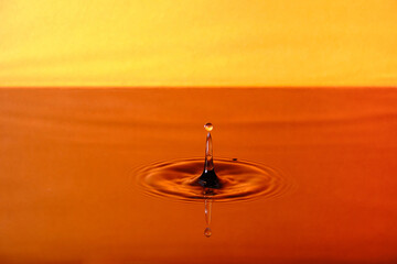 Splash drop of water with diverging water circles, on orange background.