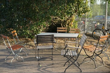 Sitzecke mit Holzstühlen und Tisch auf grauem Pflastersteinplatz vor grünem Baum im Garten bei...