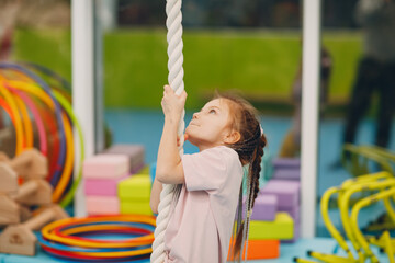 Kids doing exercises climbing tightrope in gym at kindergarten or elementary school. Children sport...