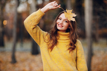 Young woman model in autumn park with yellow foliage maple leaf at face. Fall season fashion