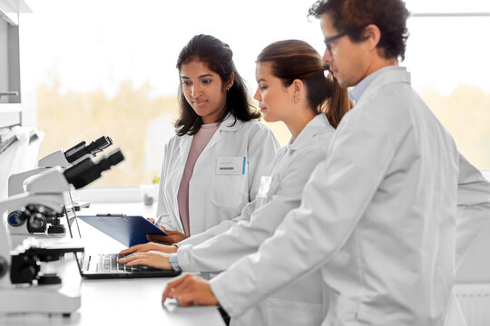 science research, work and people concept - international team of scientists with microscopes and laptop computer working in laboratory