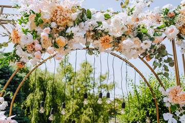 A beautiful arch decorated with flowers and lamps stands in the park at the wedding ceremony....