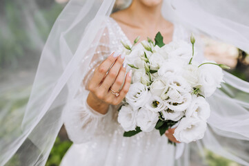 The bride in a white dress holds a bouquet of roses in her hands. Wedding portrait, photography.