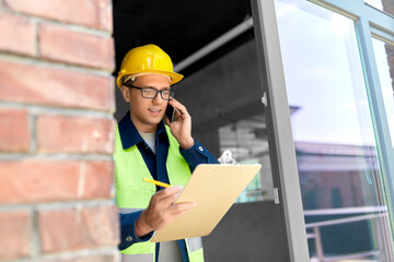 construction business and building concept - happy smiling male builder in helmet and safety west...