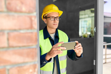 construction business and building concept - male builder in helmet and safety west with smartphone...