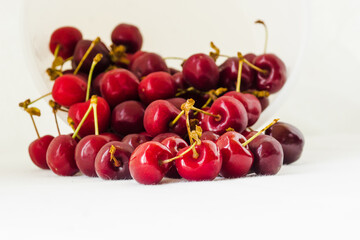 Obraz na płótnie Canvas Red cherries on a white fabric background. Many sweet cherries closeup. Juicy organic red cherries for jam, juice, smoothies, compote, desserts and cakes. Healthy eating and food concept