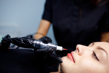 Cosmetologist applying red permanent make up tattoo on young woman lips. - obrazy, fototapety, plakaty