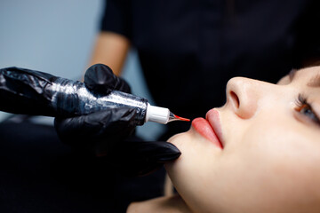 Cosmetologist master apply red permanent lips tattoo on young woman
