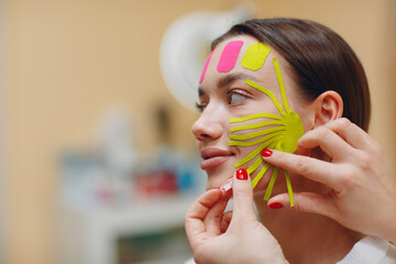Beautiful woman applying tape lifting treatment procedure on face