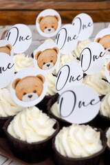 many cupcakes with white cream and toppers with bears and text one. the first birthday of the child