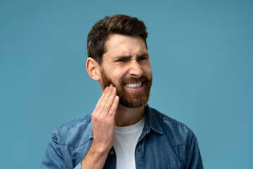 Frustrated bearded man touching cheek and wincing in pain feeling terrible tooth ache