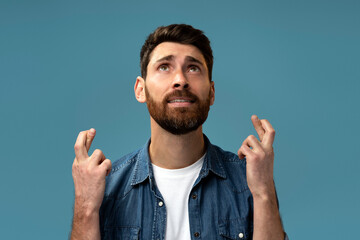 Funny hopeful man with beard crossing fingers for luck, making a wish, dreaming of innermost