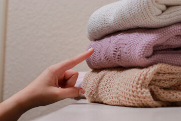female hand grabbing a sweater, stack of folded knitwear