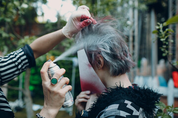 hairdresser stylist make-up artist dyes the hair of a young man with a closed face from an aerosol...