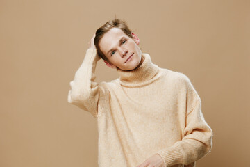 portrait of a handsome guy in a long oversized beige sweater fixing his hair