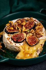  Baked brie with nuts and figs in a green bowl. Close up.