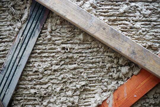 Braun-graue Lehmfassade mit Muster hinter Holzbalken 