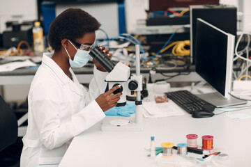 Scientist african american woman in face mask and gloves working in laboratory with electronic tech instruments and microscope. Research and development of electronic devices by color black woman.