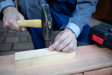 Close up of hands of carpenter holding hammer and knocking in nail the wood