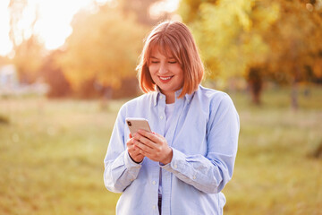 Photo portrait female student in blue shirt keeping cellphone browsing internet walking along summer park