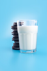 Delicious sweet black chocolate chip cookies with glass of milk filling isolated on blue background. Oat, healthy cookies and milk cup, breakfast concept