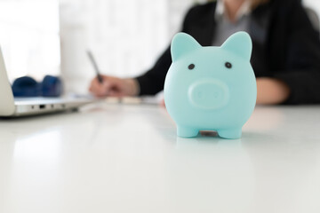 Close up of blue piggy bank on the desktop and business woman working on background