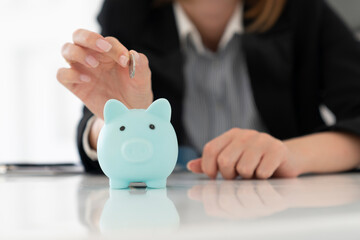 Close up photo of piggy bank and business woman putting coin in it in the office