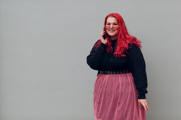European plus size woman speaking mobile phone. Young red pink haired body positive girl.