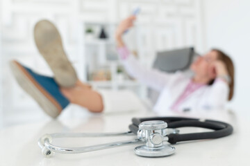 Close up photo of stethoscope on desktop and relaxing female doctor on background