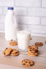 Flatlay an after school snack of chocolate chip cookies and an glass cup of milk, bottle of milk. The cookies with chocolate drops and on a rustic wood kitchen table, with copy space. yummy and tasty