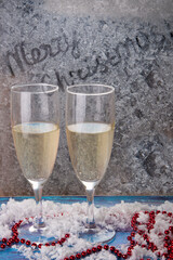 Merry Christmas title inscriptions on winter frozen window. Two champagne glasswines on windowsill