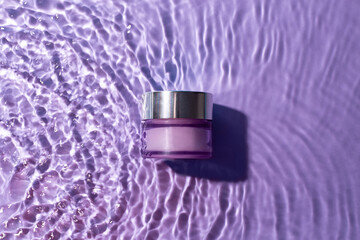 Purple cosmetic jar on the purple water surface. Blank label for branding mock-up. Summer water pool fresh concept. Flat lay, top view..