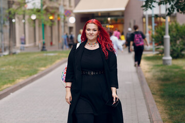 European plus size woman walking outdoor street city. Young red pink haired body positive girl.